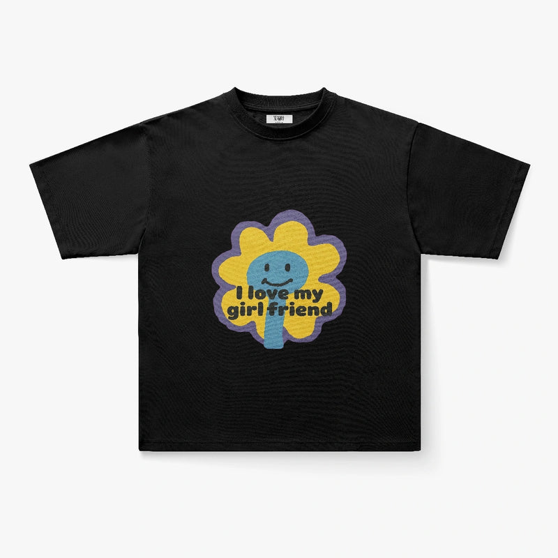 The I Love My Girlfriend Retro Flower Smiley Graphic Oversized Tee is a black shirt with a cartoon daisy, smiling face, and yellow “I love my girlfriend” text across the flower.