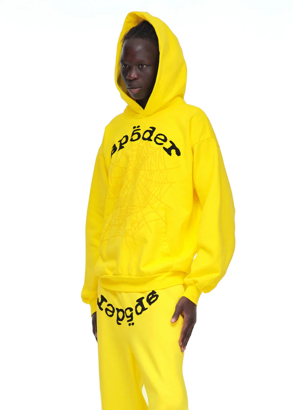 A person wears the Yellow Graphic Hoodie with Spider Web Print and Lettering – Comfort Fit Pullover Hoodie and matching sweatpants, both featuring wavy "spɒɘdɘɿ" text and a spider web print on the front.