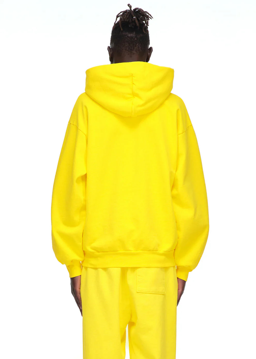 A person with dark hair in short twists is shown from behind, wearing the Yellow Graphic Hoodie with Spider Web Print and Lettering – Comfort Fit Pullover Hoodie against a plain white background.
