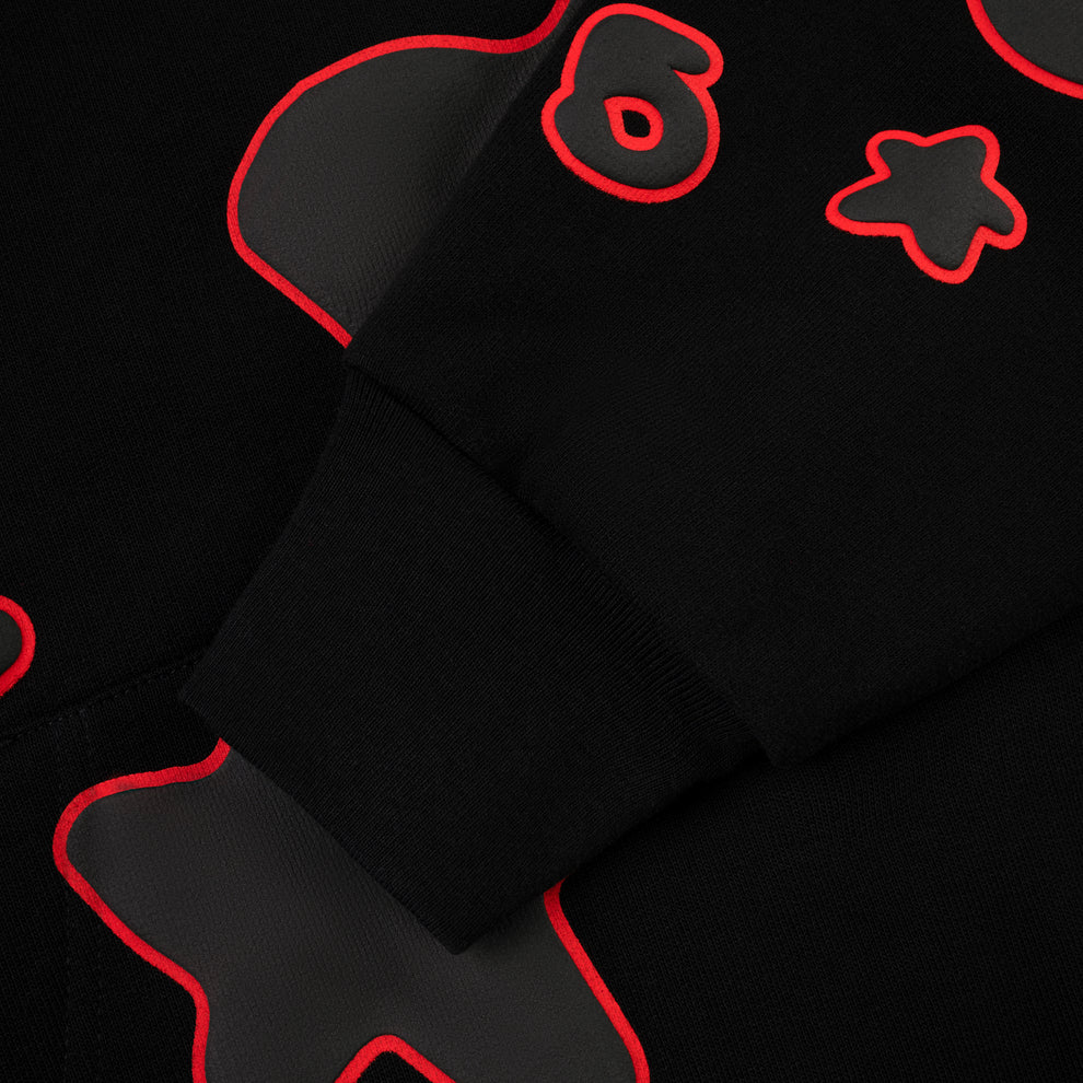 A close-up of the Sp5der 440GSM Heavyweight Star Hoodie—Black & Grey Oversized Streetwear Pullover—shows abstract red and gray outlined shapes, a star, the number 6, and a ribbed sleeve cuff.