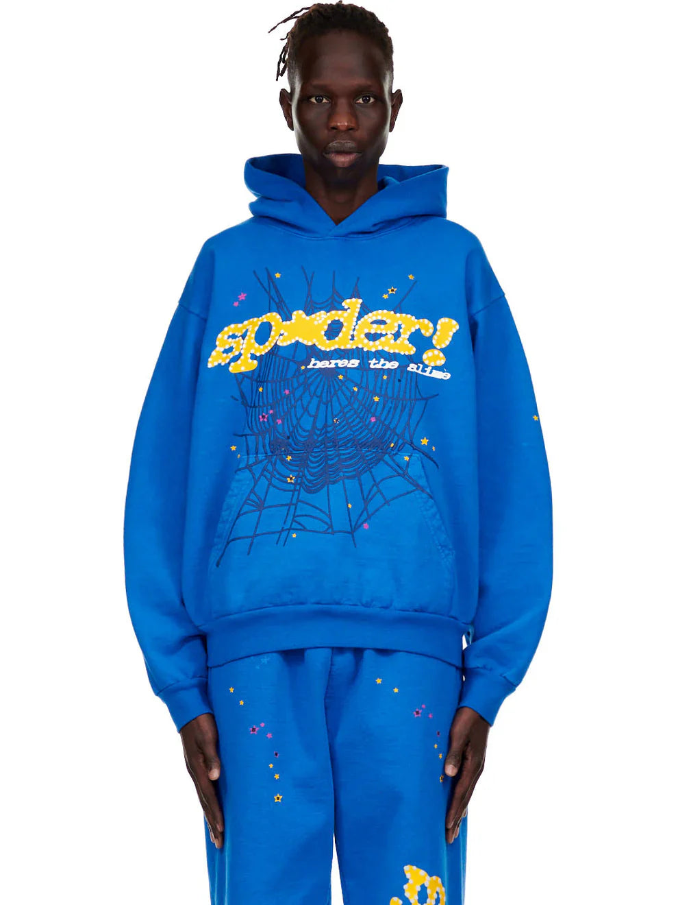 A person wearing the Sp5der “Hares the Slime” Hoodie (440GSM) in royal blue with a fuzzy logo and spider-web graphic stands against a plain white background.