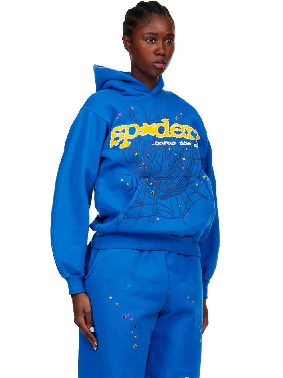 A person wears the Sp5der “Hares the Slime” Hoodie (440GSM) in royal blue, featuring a fuzzy logo and spider-web graphic, with matching sweatpants displaying yellow Sp5der text and colorful splatters, standing against a white background.