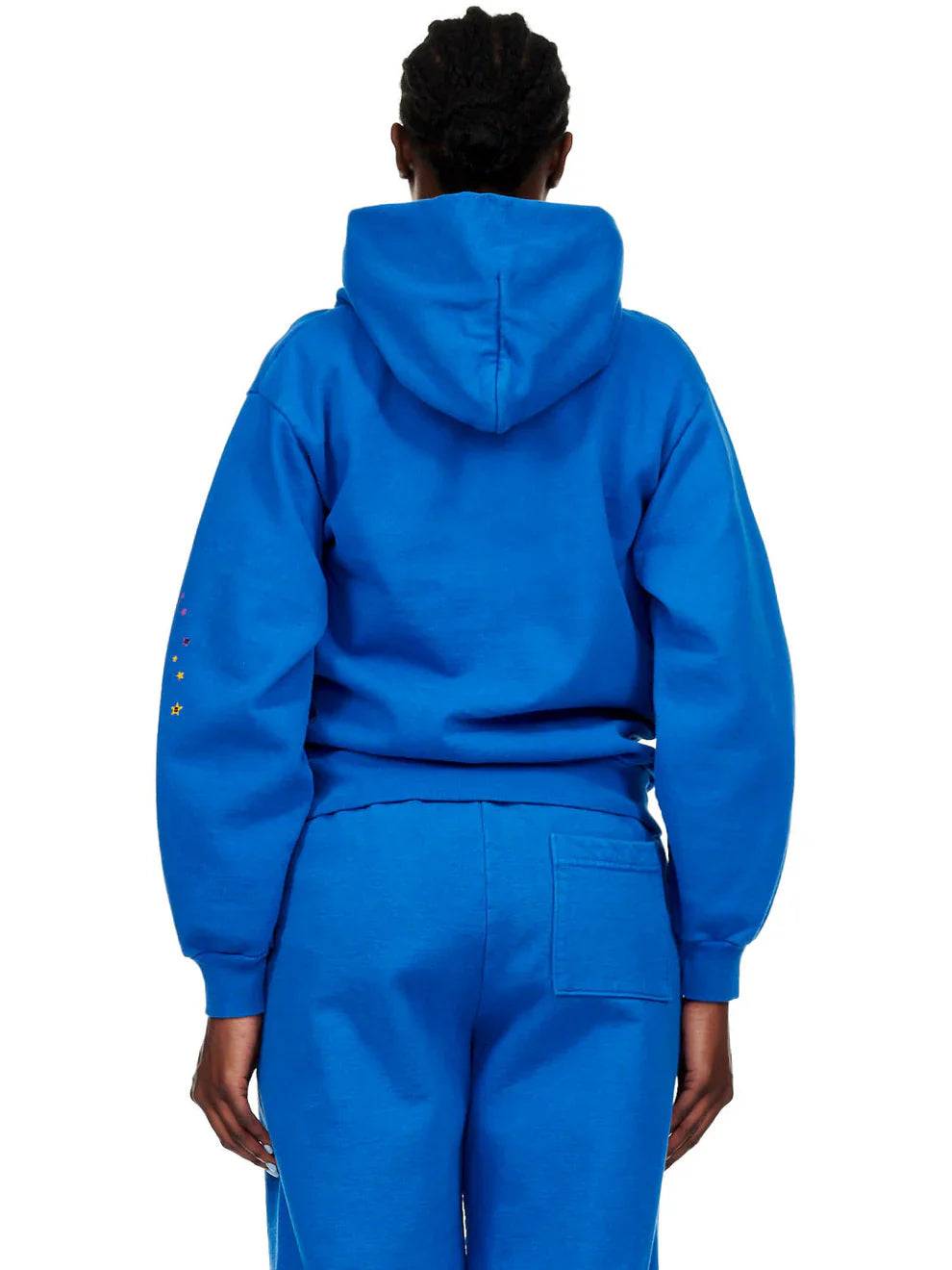 A person stands with their back to the camera wearing a Sp5der “Hares the Slime” Hoodie (440GSM) – Royal Blue, featuring a fuzzy logo spider-web graphic and hood up, paired with matching sweatpants.