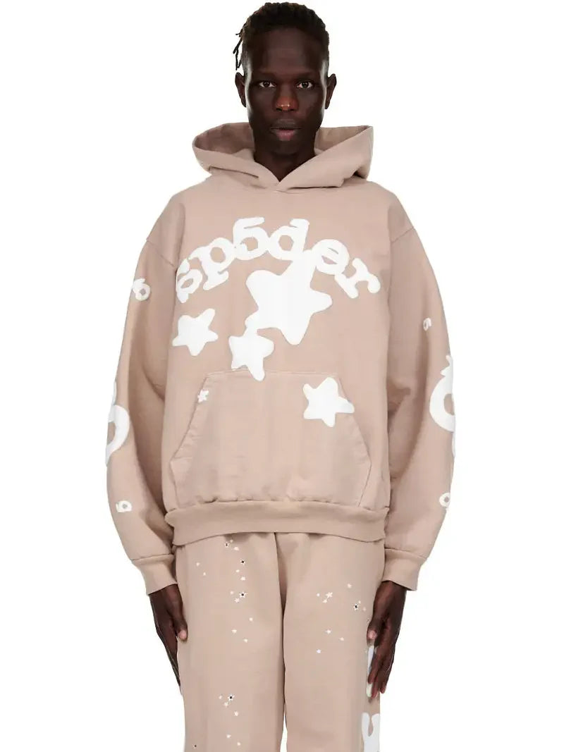 A person stands against a white background wearing the Sp5der Star Hoodie – Brown & White 440GSM Heavyweight Oversized Streetwear Pullover with matching pants, both featuring bold white star and circle designs on brown fleece.