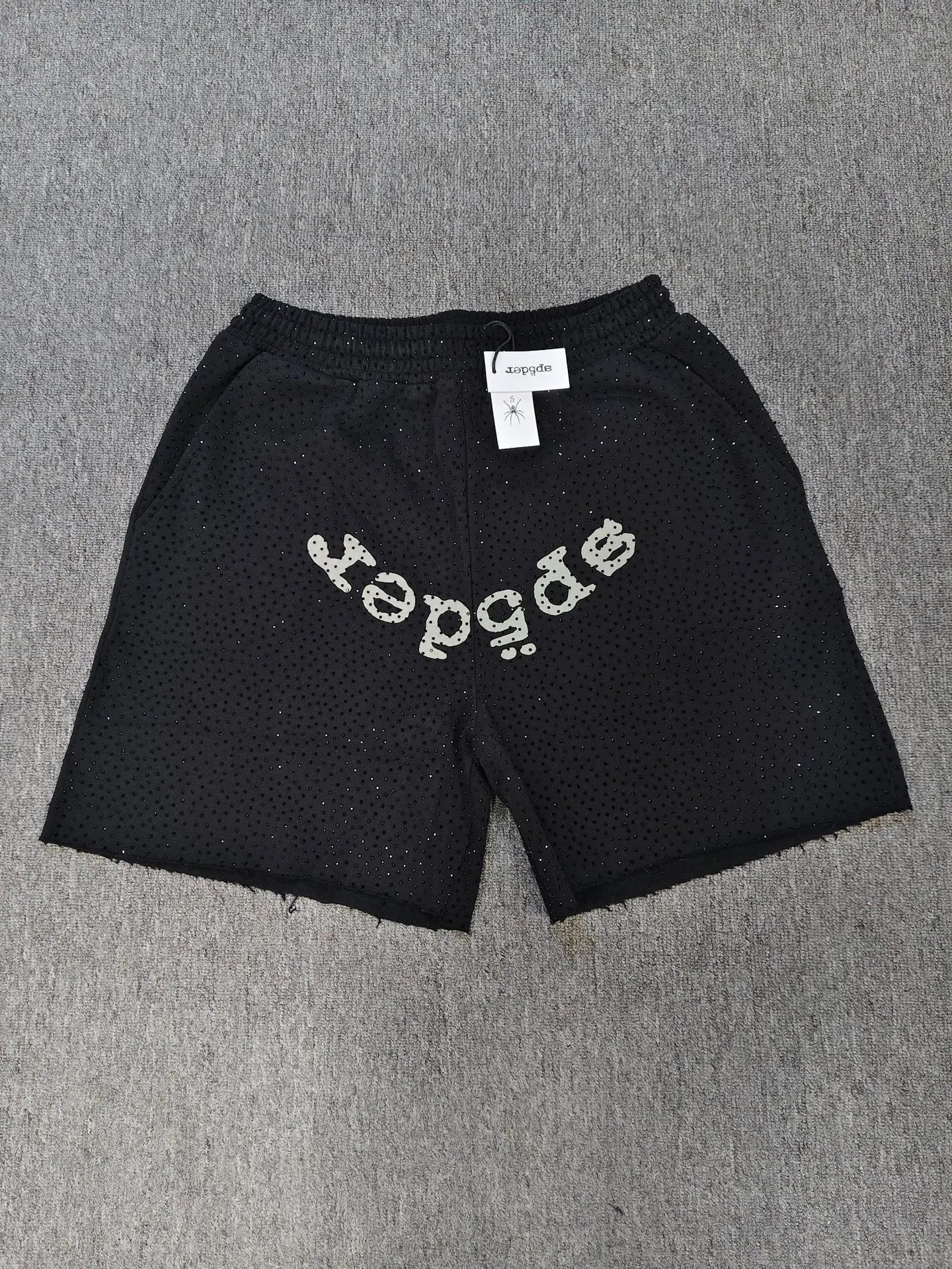 Black Sp5der shorts featuring a front curved logo graphic and raw hems.