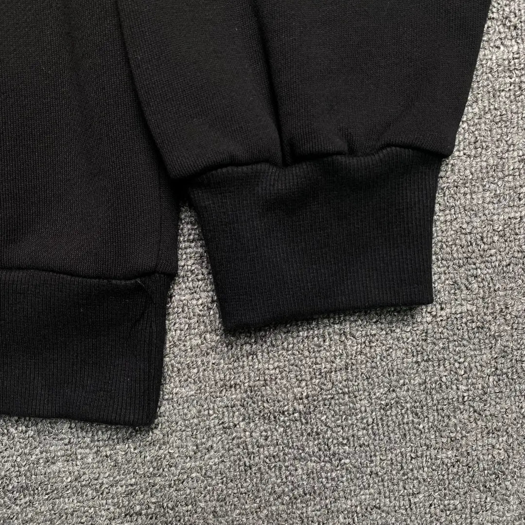 Close-up of the cuffs and waistband of the Black Sp5der Web Hoodie 440GSM – Black Spider Hoodie Purple Web White Stars Core, shown lying on a textured gray carpet.
