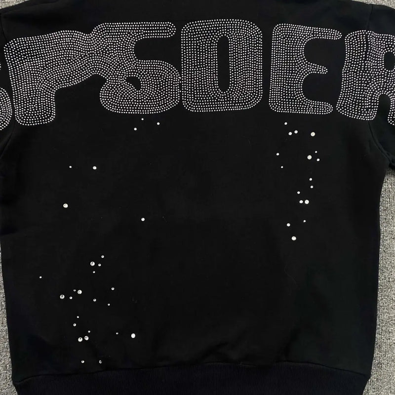 The Sp5der Black Rhinestone Spiderweb Crystal Hoodie features bold lettering with rhinestone outlines across the back and scattered crystals below, delivering a standout streetwear look.