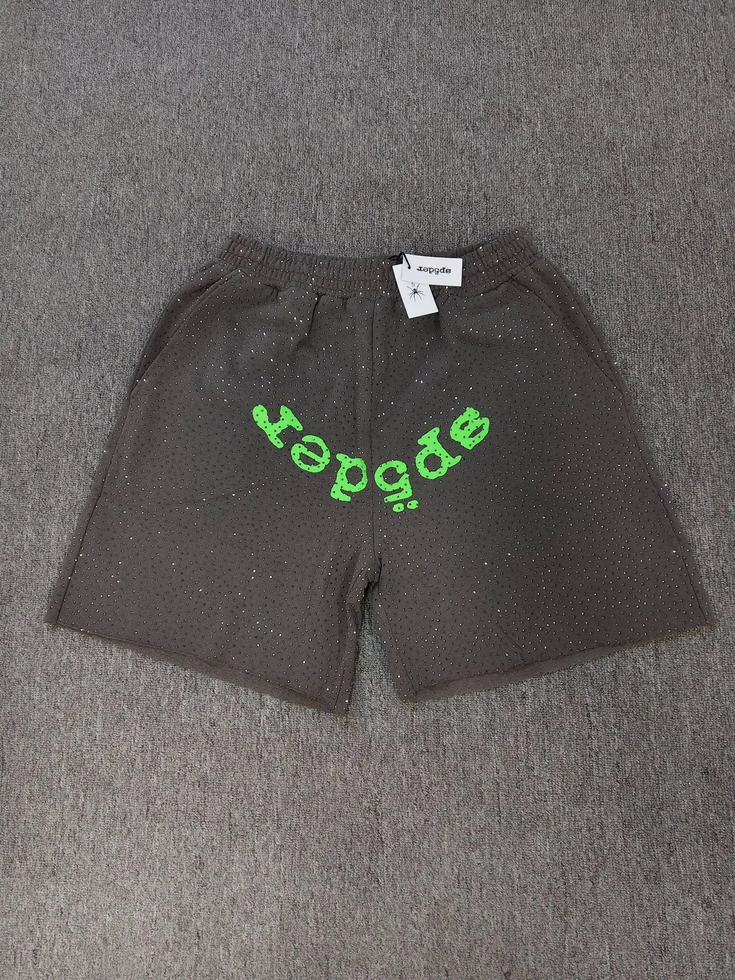 Dark gray Sp5der jogger shorts featuring a green logo graphic across the front and all-over rhinestone detailing.