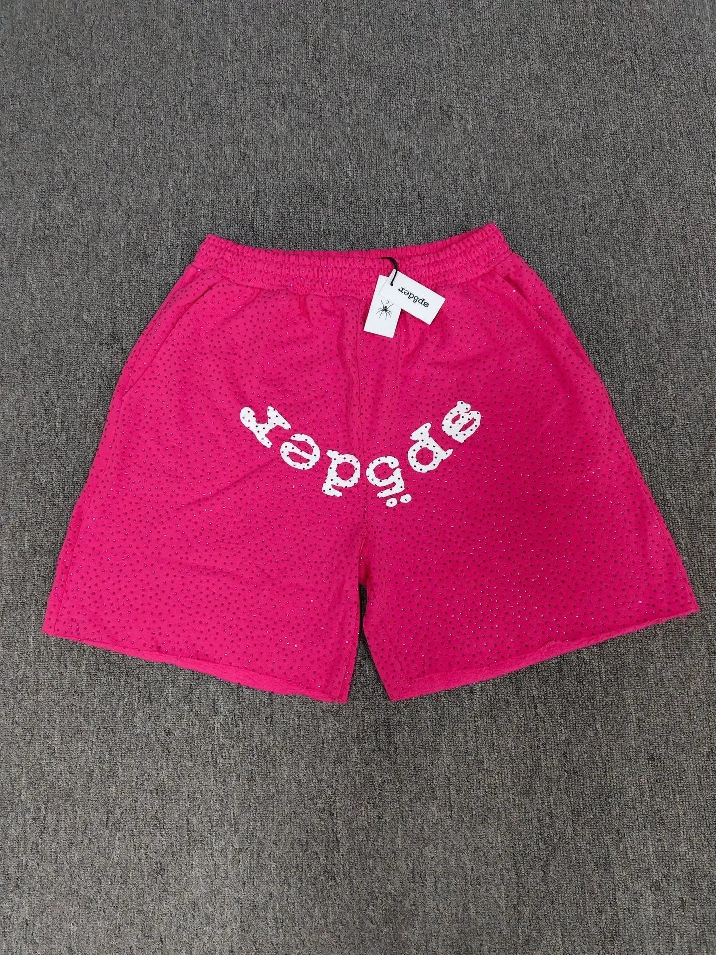 Pink Sp5der jogger shorts featuring a white front logo graphic and all-over rhinestone embellishments.