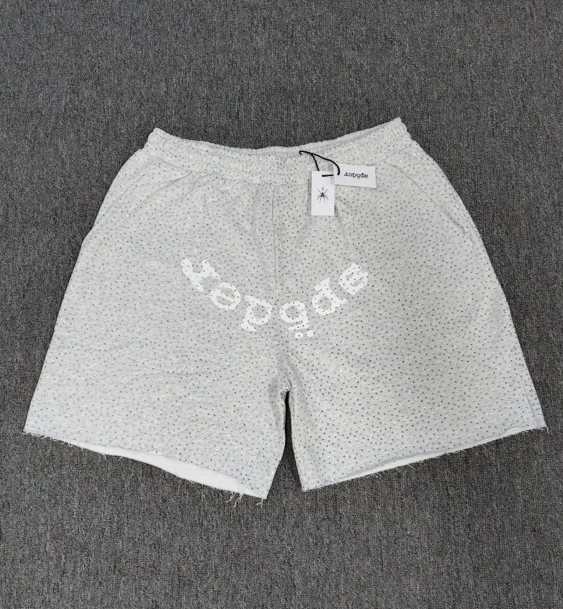 Light gray Sp5der sweat shorts featuring all-over rhinestone detailing, a white arched front logo, elastic waistband, and raw hem.