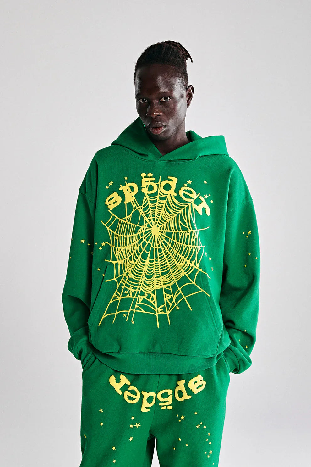 A person wears the Sp5der Web Hoodie – Emerald Green & Yellow 440GSM Heavyweight Oversized Streetwear Pullover with matching pants, featuring bold yellow spider web graphics and a stylized "sp5der" font, set against a plain gray background.