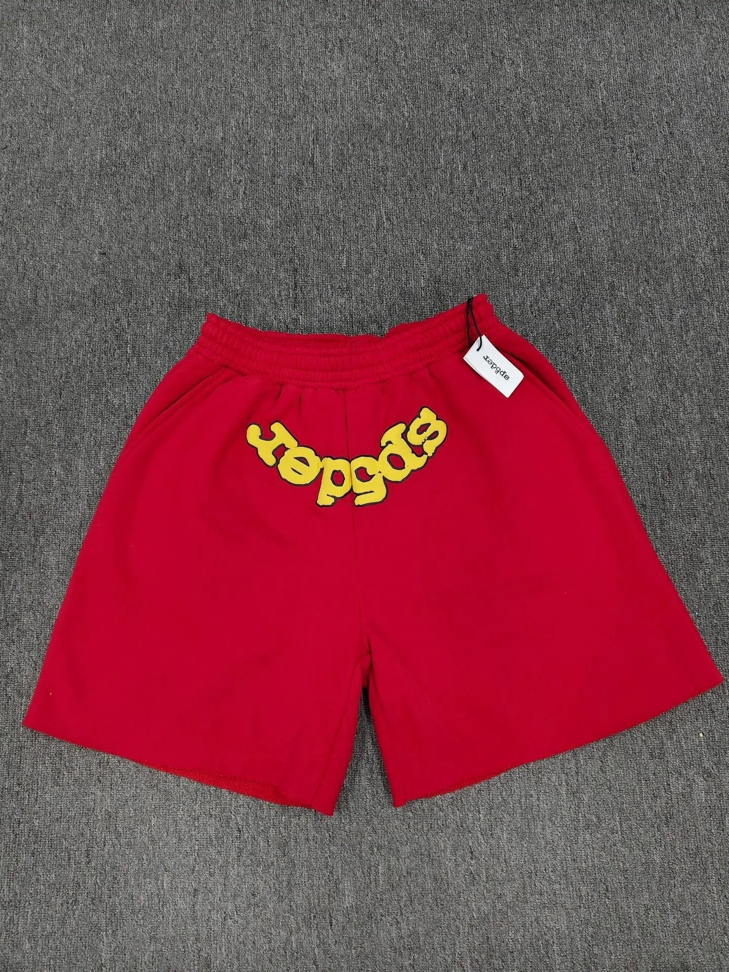 Red Sp5der jogger shorts with yellow embroidered letter graphic on the front, laid flat