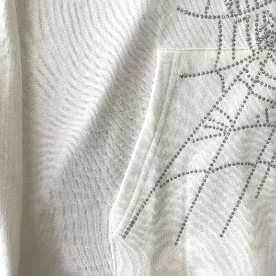 A close-up of the White Sp5der Crystal Web Hoodie 440GSM pocket, featuring luxury streetwear style with sparkling rhinestones arranged in a shimmering web pattern.