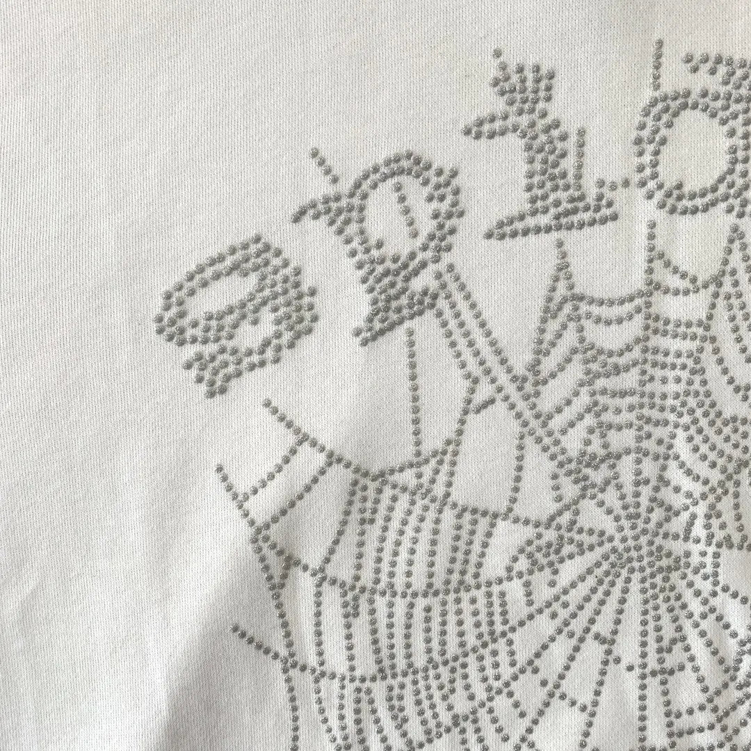 Close-up of the White Sp5der Crystal Web Hoodie 440GSM—white fabric with raised silver rhinestones in a web pattern and a partial “spider” detail, showcasing premium luxury streetwear craftsmanship.