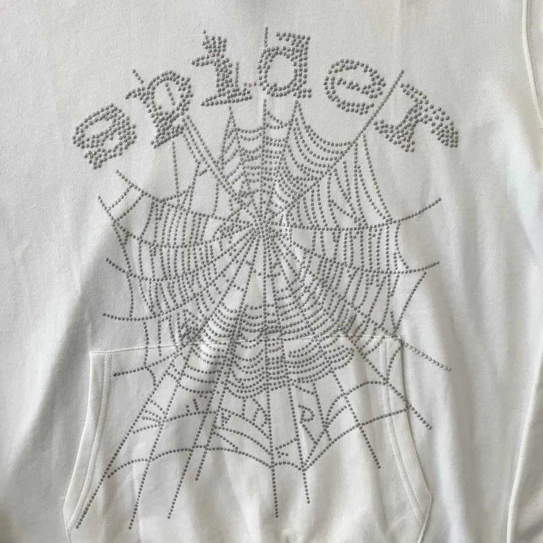The White Sp5der Crystal Web Hoodie 440GSM features white fabric with "spider" and a large spiderweb, both made from silver rhinestones. This luxury streetwear hoodie draws inspiration from the iconic sp5der design, displayed above the front pocket.