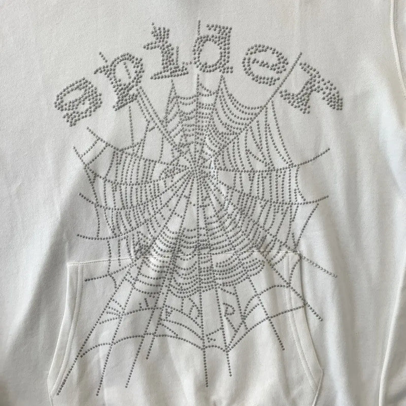 The White Sp5der Crystal Web Hoodie 440GSM features white fabric with "spider" and a large spiderweb, both made from silver rhinestones. This luxury streetwear hoodie draws inspiration from the iconic sp5der design, displayed above the front pocket.