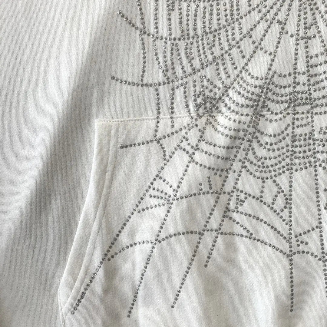 Close-up of the White Sp5der Crystal Web Hoodie 440GSM, a luxury white rhinestone spider hoodie featuring a front pocket and decorative crystal web pattern crafted from shiny silver studs.