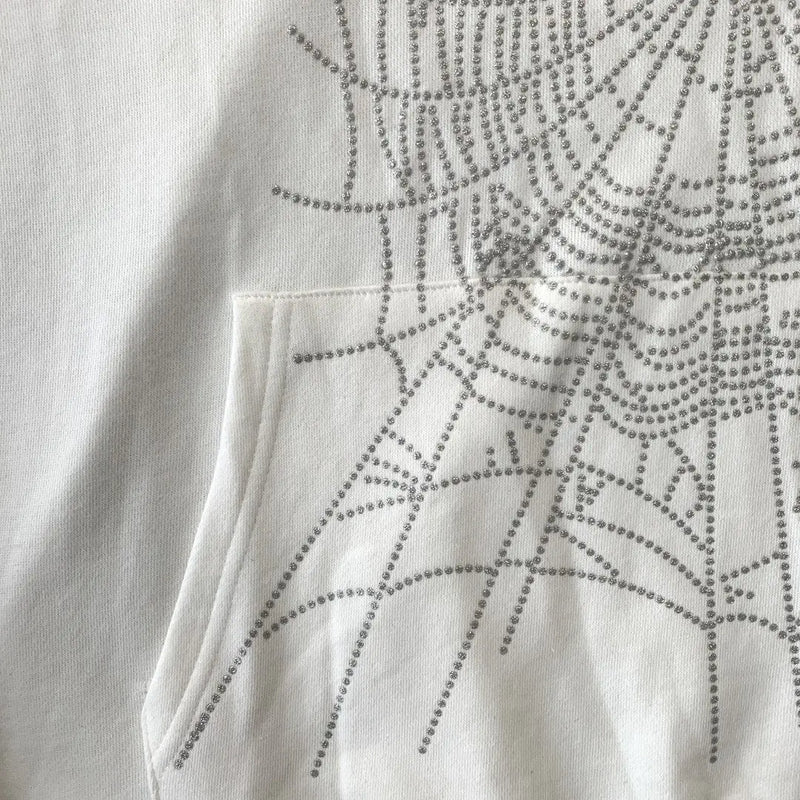 Close-up of the White Sp5der Crystal Web Hoodie 440GSM, a luxury white rhinestone spider hoodie featuring a front pocket and decorative crystal web pattern crafted from shiny silver studs.