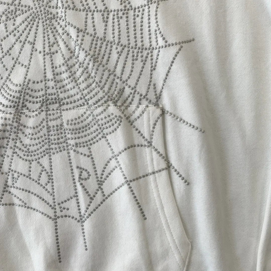 Close-up of the White Sp5der Crystal Web Hoodie 440GSM, showing its white fabric with a crystal rhinestone spiderweb pattern inspired by luxury streetwear trends.