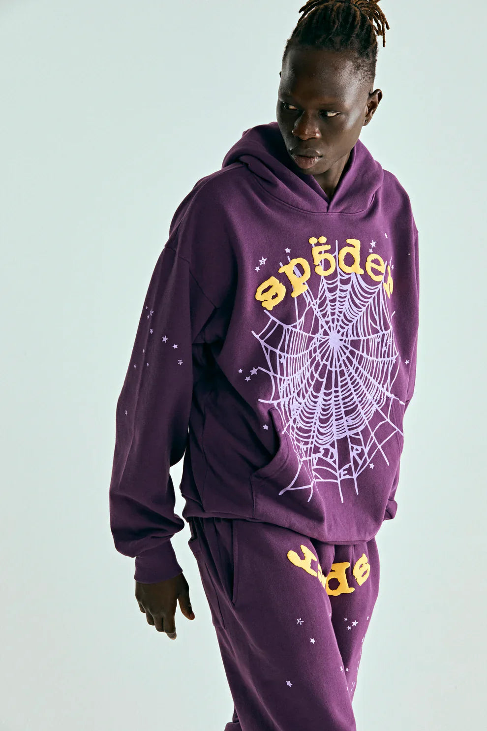 Wearing the Sp5der Web Hoodie – Deep Purple & Yellow 440GSM Heavyweight Oversized Streetwear Pullover, someone stands against a light background, bold whiteweb and yellow accents offering a standout nod to luxury streetwear.