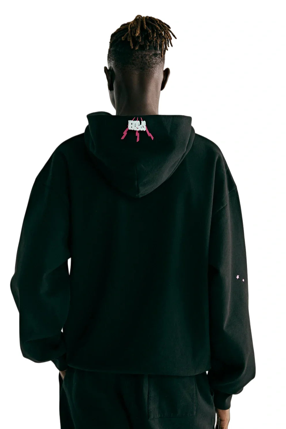 Seen from behind against a plain white background, a person with short, twisted hair wears the Sp5der 555 Hoodie – Black & Pink Web 440GSM Heavyweight Streetwear Pullover featuring pink gun graphics on the hood—a bold Y2K-inspired statement.