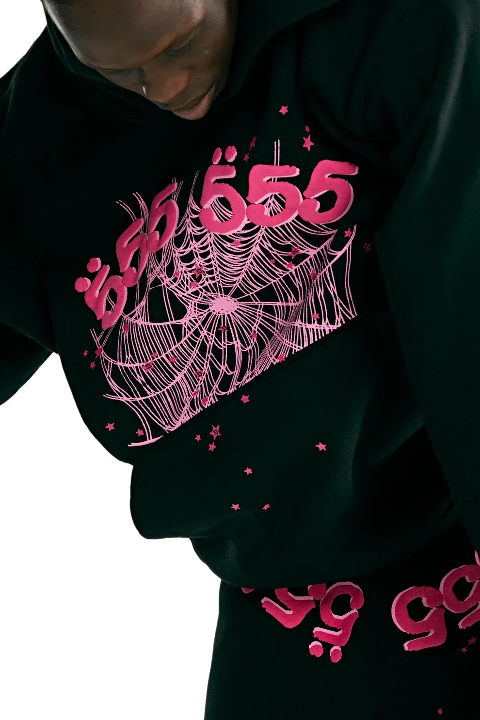 Wearing the Sp5der 555 Hoodie – Black & Pink Web 440GSM Heavyweight Streetwear Pullover with bold pink lettering, web graphics, and stars epitomizes Y2K-inspired luxury streetwear on a sleek white backdrop.