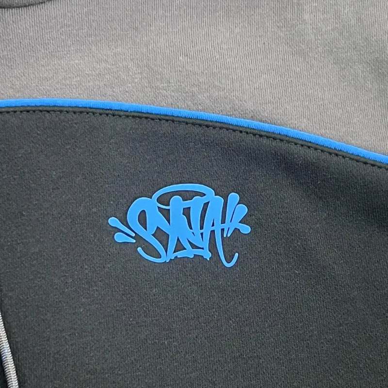 A close-up of the Syna World Black Grey Color Block Graphic Hoodie, featuring black and gray fabric with blue trim and bold blue graffiti-style "SAYAH" text for a standout streetwear look.