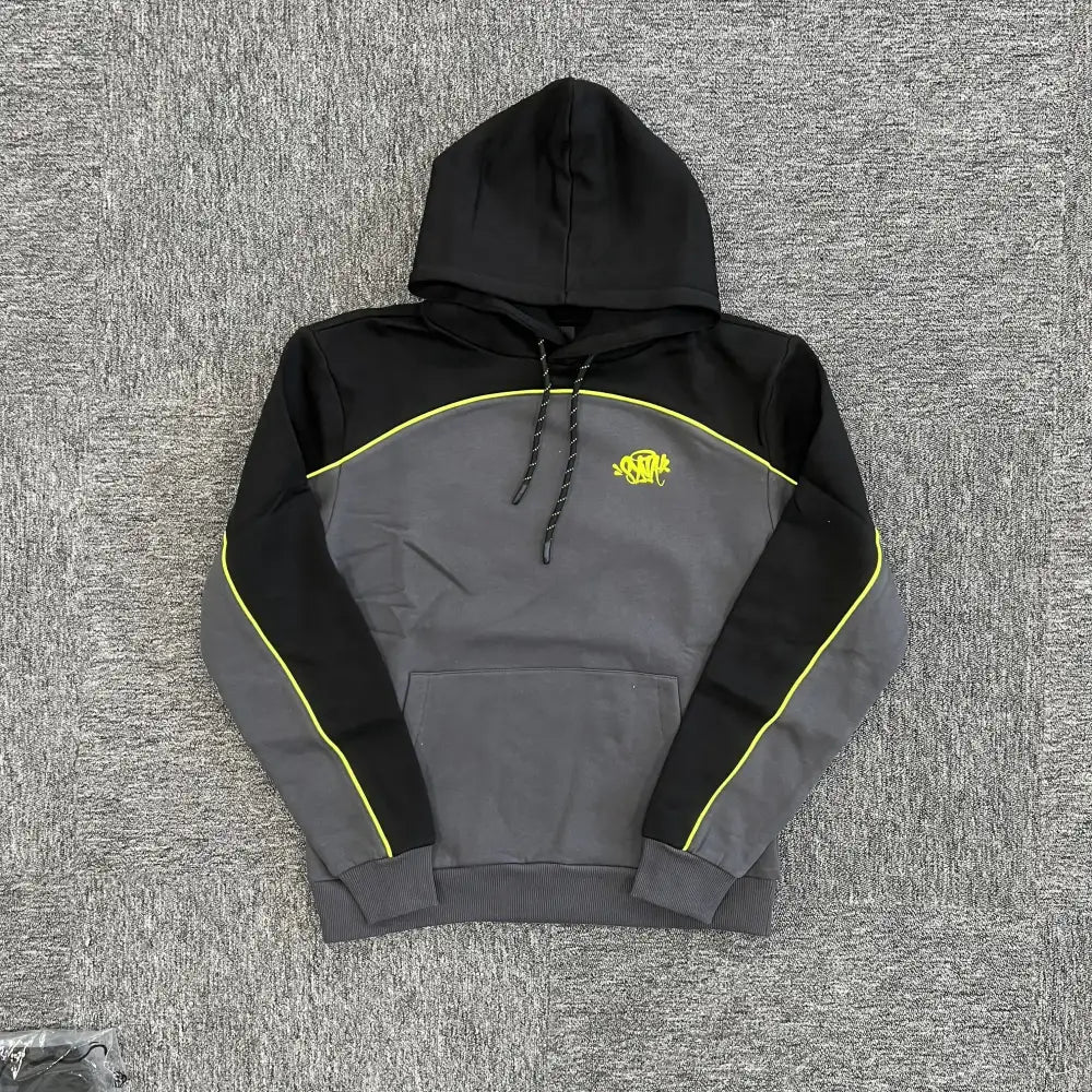 Syna World black and grey colorblock pullover hoodie with neon yellow piping and embroidered chest logo, laid flat