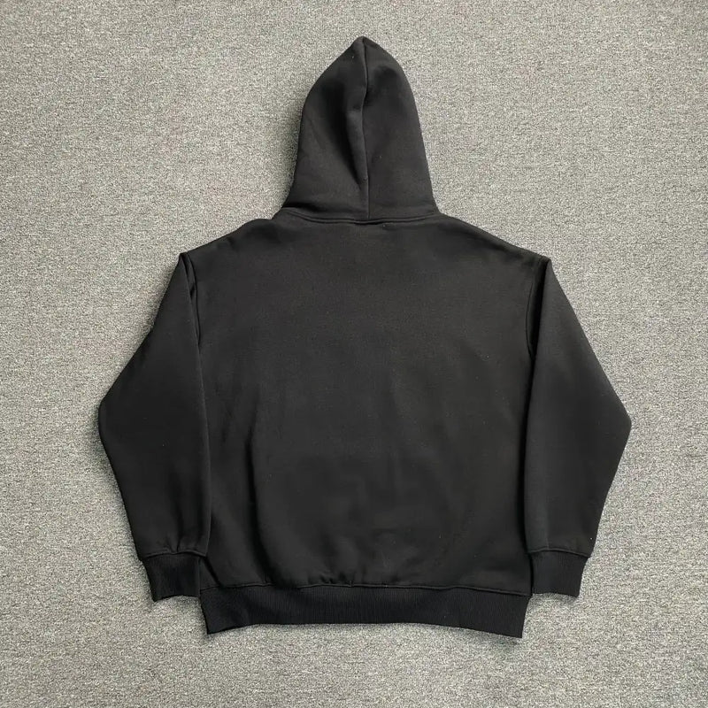 The Syna World Black Yellow Graffiti Graphic Oversized Hoodie is laid flat on a grey carpet, shown from the back with the hood up and sleeves spread out for a classic streetwear vibe.