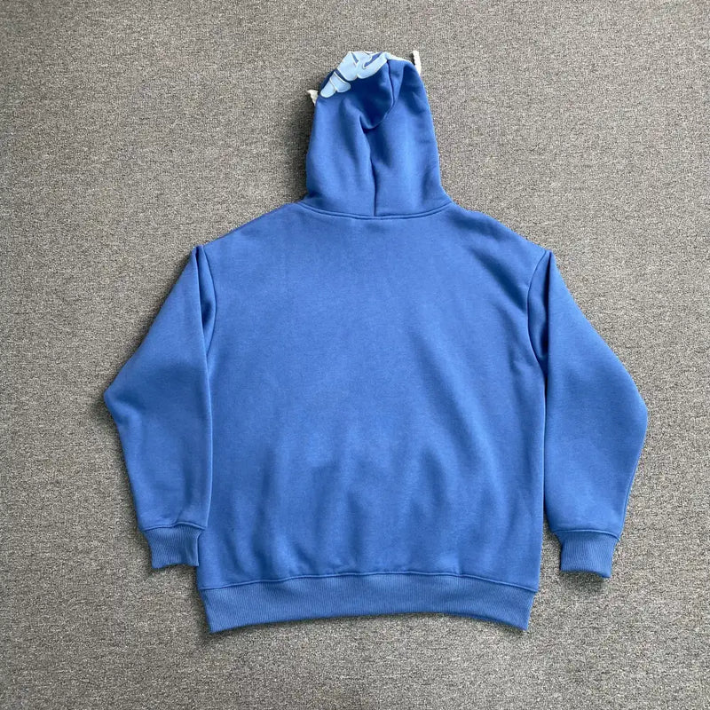 The Syna World Blue Letter Print Hoodie, made of cotton-polyester, is shown from the back lying flat on a gray carpet. The hoodie features playful light blue plush ear-like details on the hood for a cozy, fun look.
