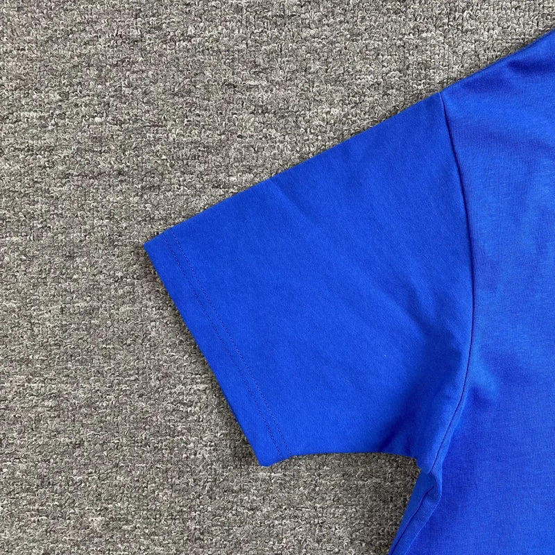 A close-up of the right sleeve and shoulder of the Syna World Blue White Front Graphic Crew Neck T-Shirt, perfect for streetwear, laid flat on a textured gray surface.