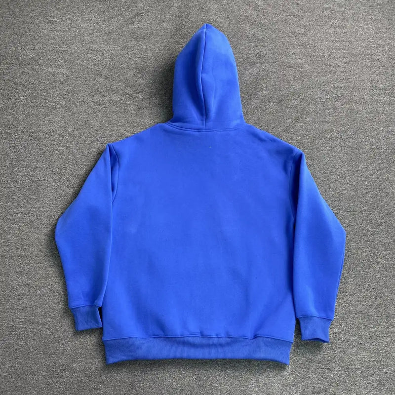 The Syna World Blue Graffiti Letter Print Hoodie is laid flat on a gray carpet, shown from the back with hood up and sleeves spread—an eye-catching streetwear piece ideal for casual style.