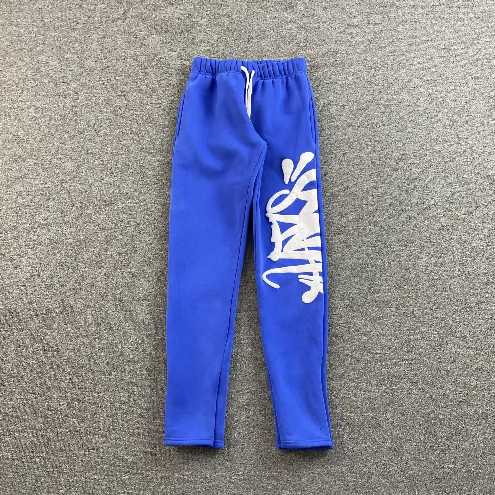Blue jogger pants with white graffiti graphic print on right leg and white drawstring waistband
