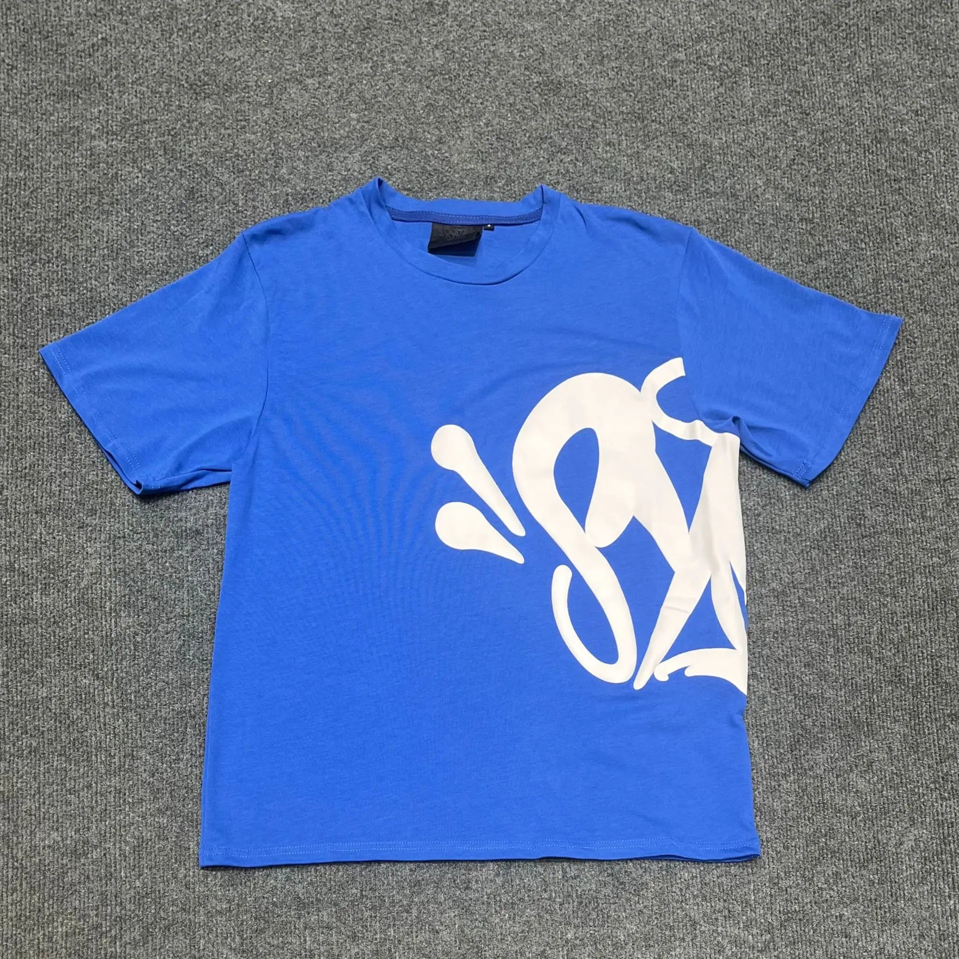 Blue Syna World short-sleeve crew neck T-shirt with white abstract front graphic print, laid flat on grey surface