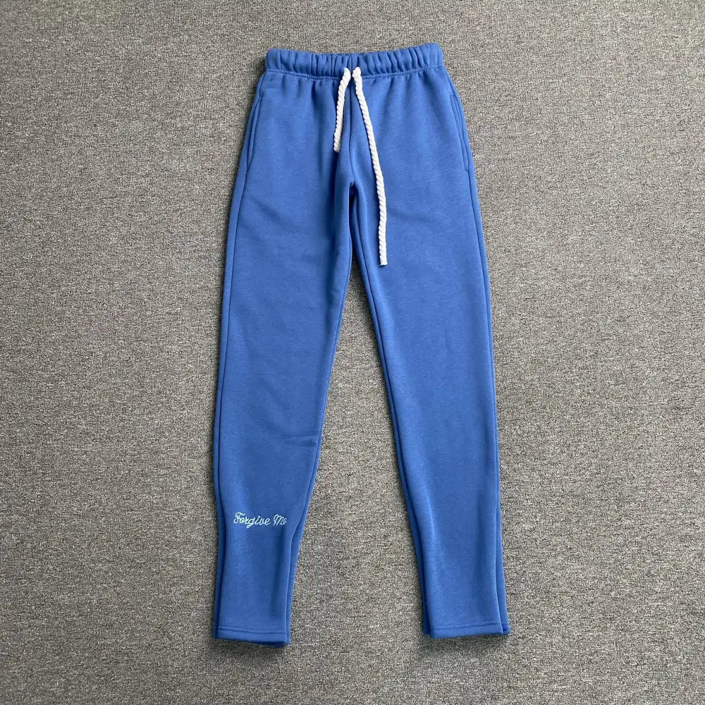 Blue Syna World jogger pants with white rope drawstring and script letter print on lower left leg, flat lay view