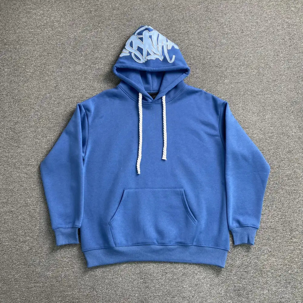 Blue Syna World pullover hoodie with graffiti letter print on hood and white rope drawstrings, laid flat