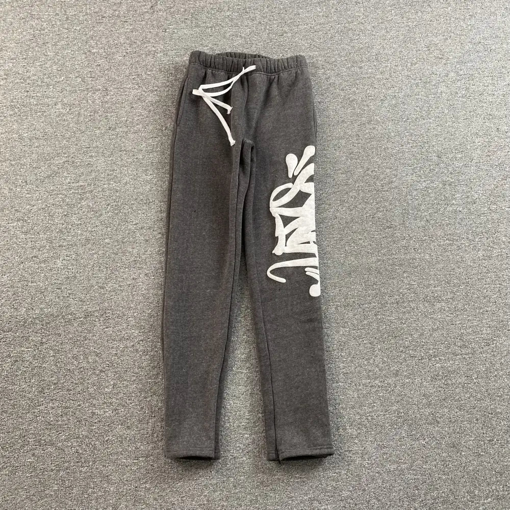 Dark gray jogger pants with white graffiti letter print on the right leg and white drawstring waistband