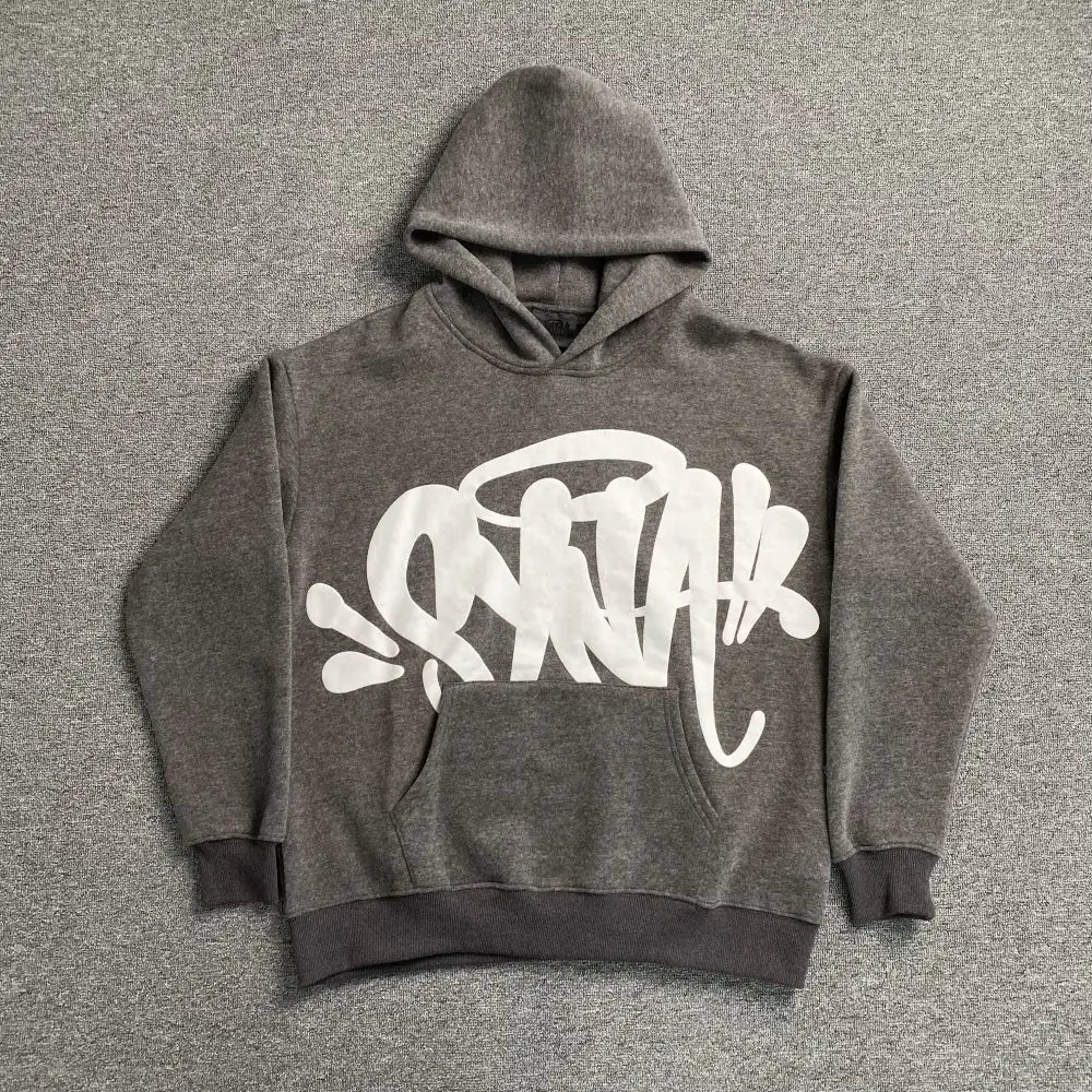 Grey pullover hoodie with white graffiti script graphic on the front chest, laid flat on a grey surface