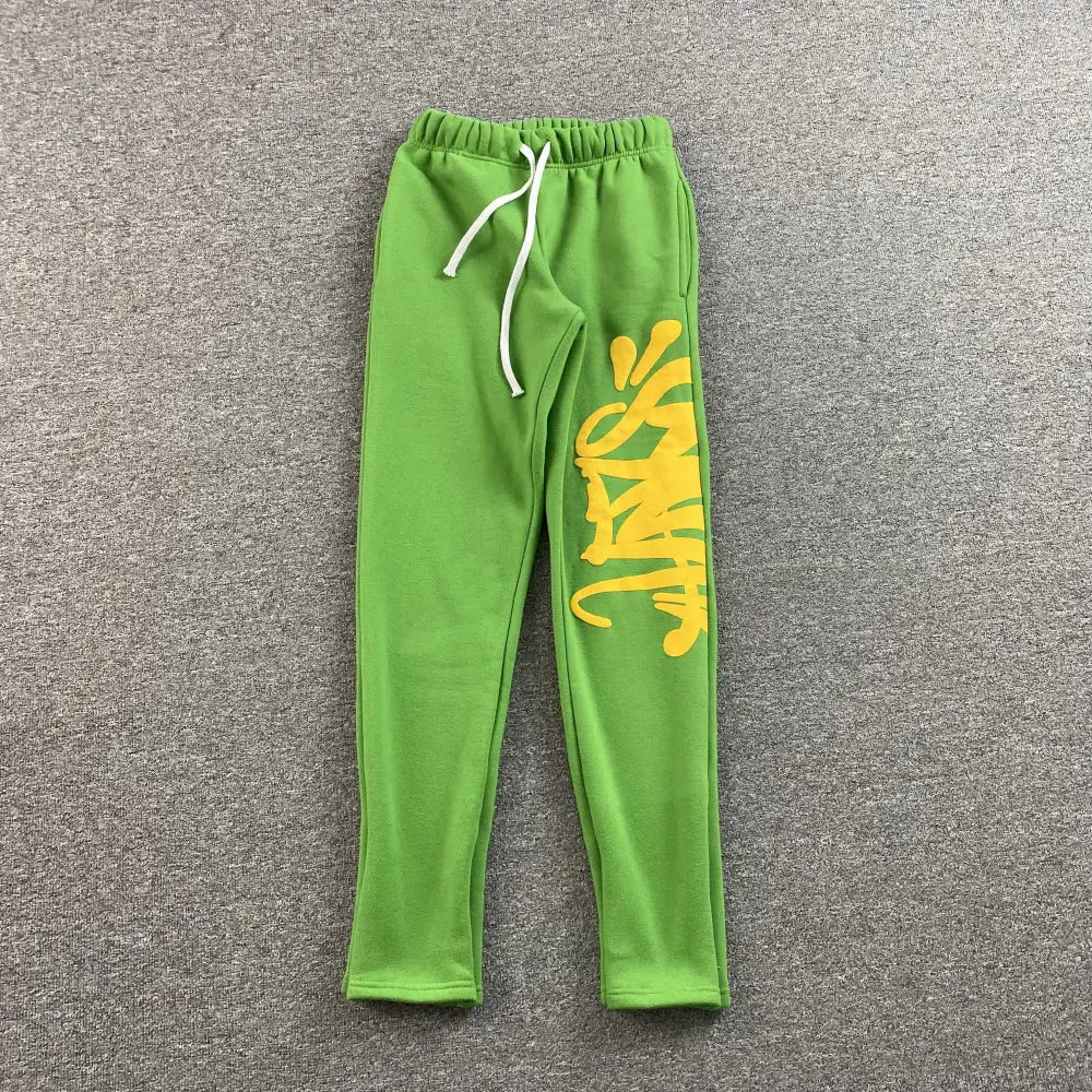 Green jogger pants with yellow graffiti letter print on the right leg and white drawstring waistband
