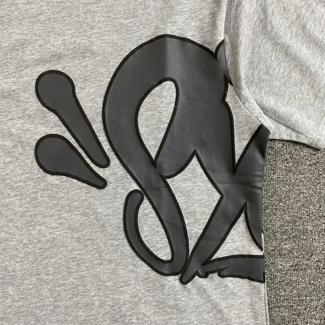 The Syna World Grey Letter Graphic Crewneck T-Shirt is made from 100% cotton and features a bold black abstract design with swooping lines and teardrop shapes across its oversized, heather grey surface.