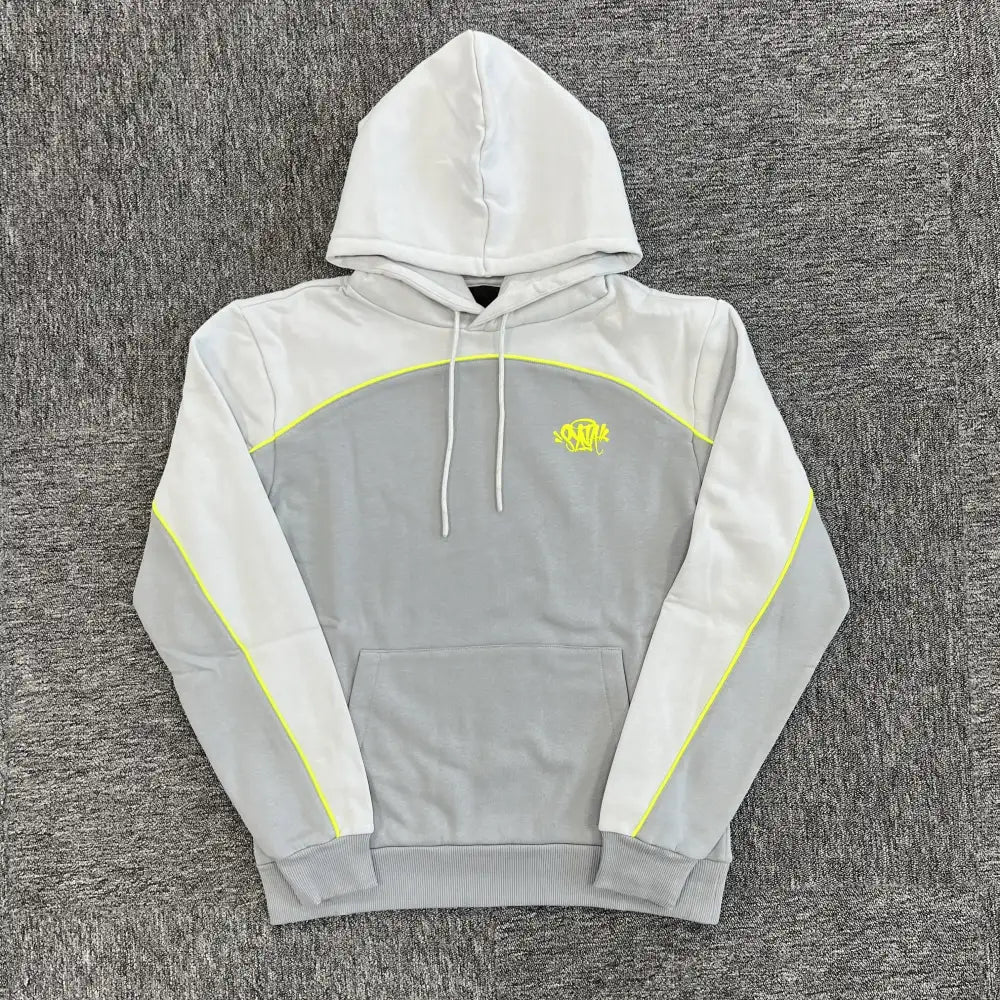 Syna World light grey and mid-grey colorblock hoodie with neon yellow seam piping and embroidered chest logo, laid flat