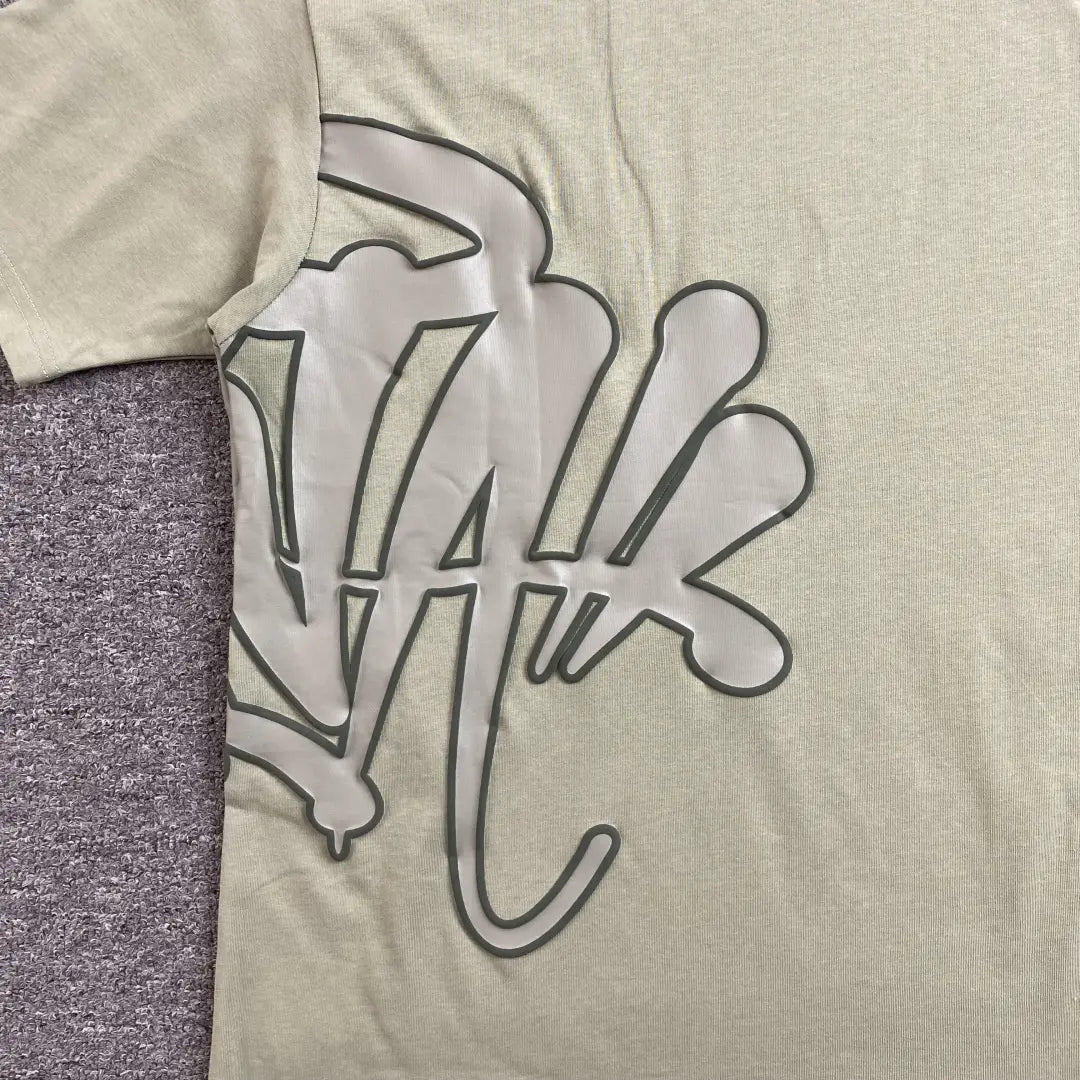 The Syna World Green Letter Graphic Crew Neck T-Shirt features bold green lettering on a stylish, relaxed fit—ideal for a streetwear-inspired look. Photographed flat on a textured gray surface.