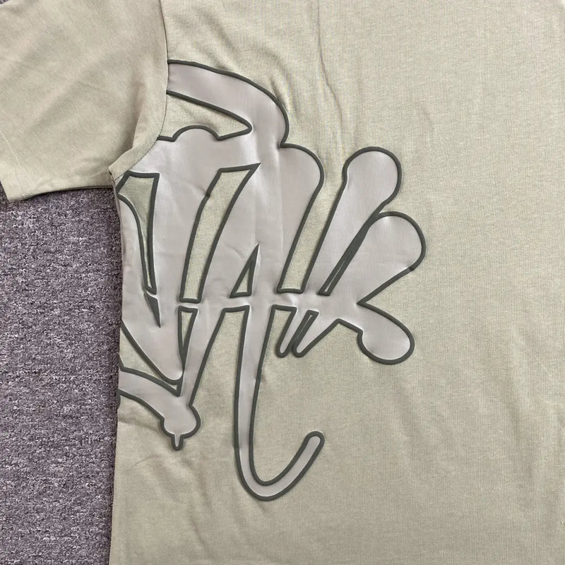 The Syna World Green Letter Graphic Crew Neck T-Shirt features bold green lettering on a stylish, relaxed fit—ideal for a streetwear-inspired look. Photographed flat on a textured gray surface.