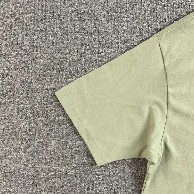 A close-up of the Syna World Green Letter Graphic Crew Neck T-Shirt lying flat on a gray textured carpet, highlighting the sleeve and torso—ideal for stylish streetwear outfits.