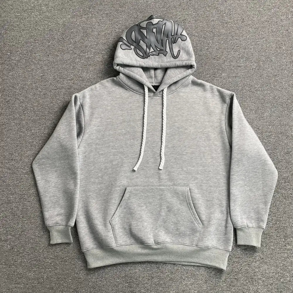 Light grey oversized hoodie with tonal graffiti print on the hood, laid flat on a grey surface