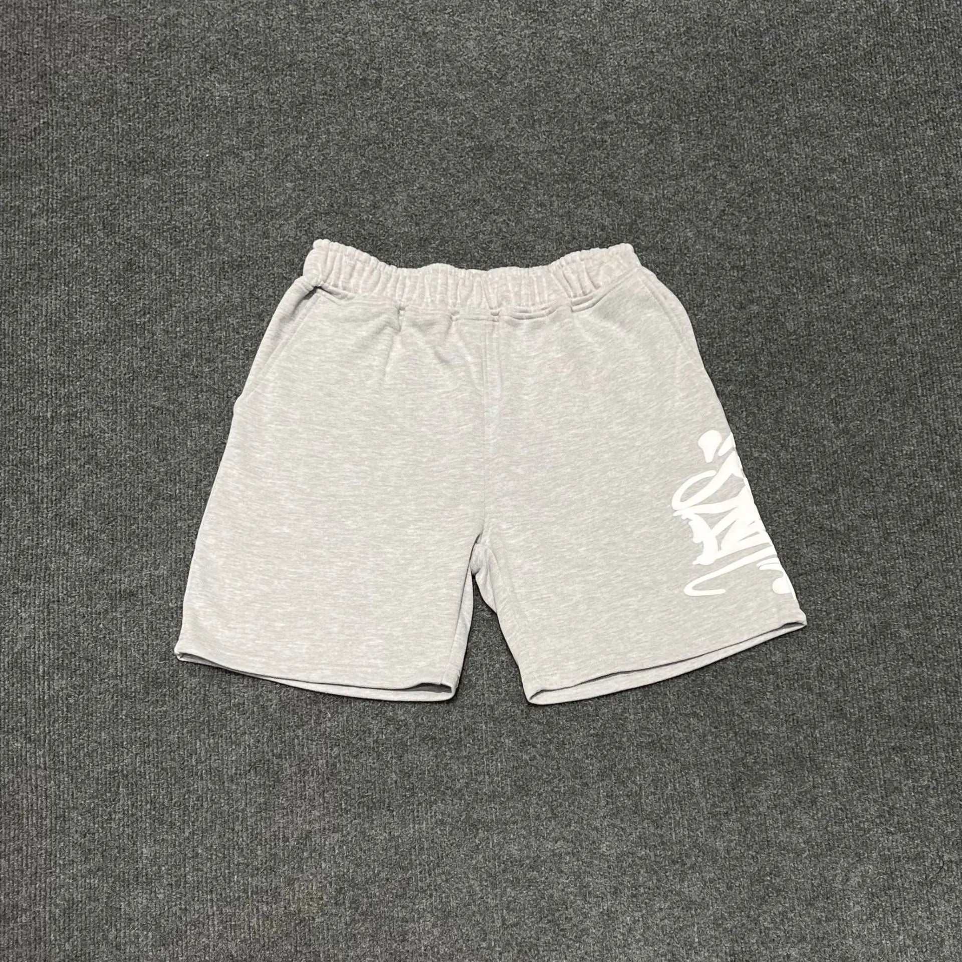 Light grey cotton jogger shorts with white graffiti letter print on the right leg and elasticated drawstring waistband