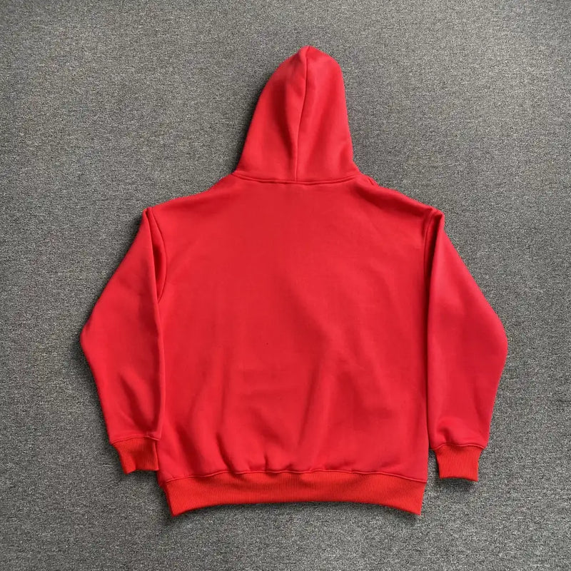 The Syna World Red Graffiti Letter Print Oversized Hoodie is shown laid flat, back facing up with the hood raised and sleeves spread on a gray carpet—an ideal streetwear pullover for casual looks.
