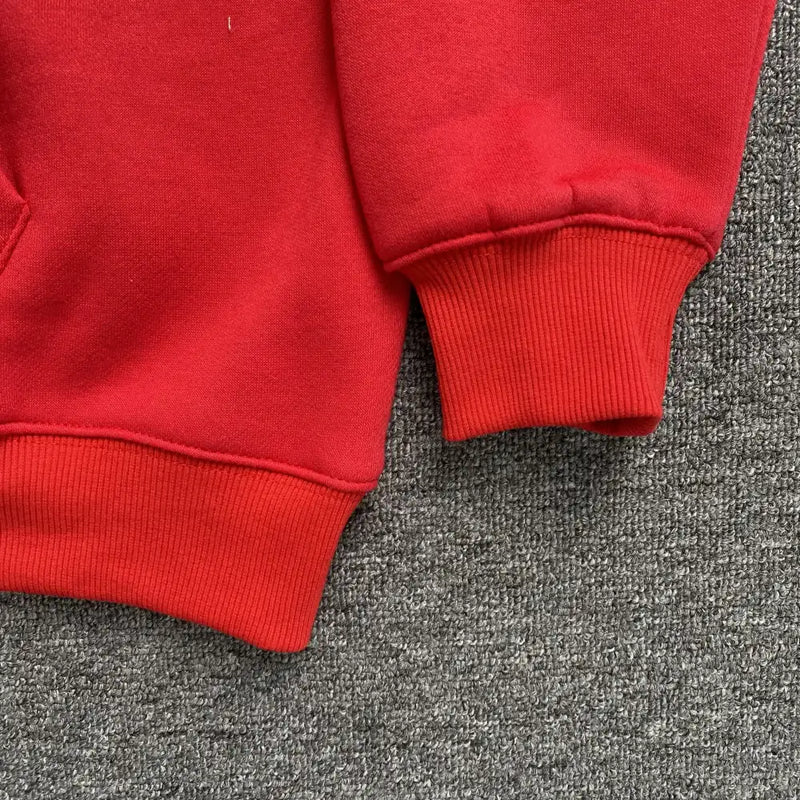 Close-up of the cuff and hem of the Syna World Red Graffiti Letter Print Pullover Hoodie on a grey textured carpet. The sweatshirt has ribbed sleeve and bottom hems, making it an ideal addition to any streetwear hoodie collection.