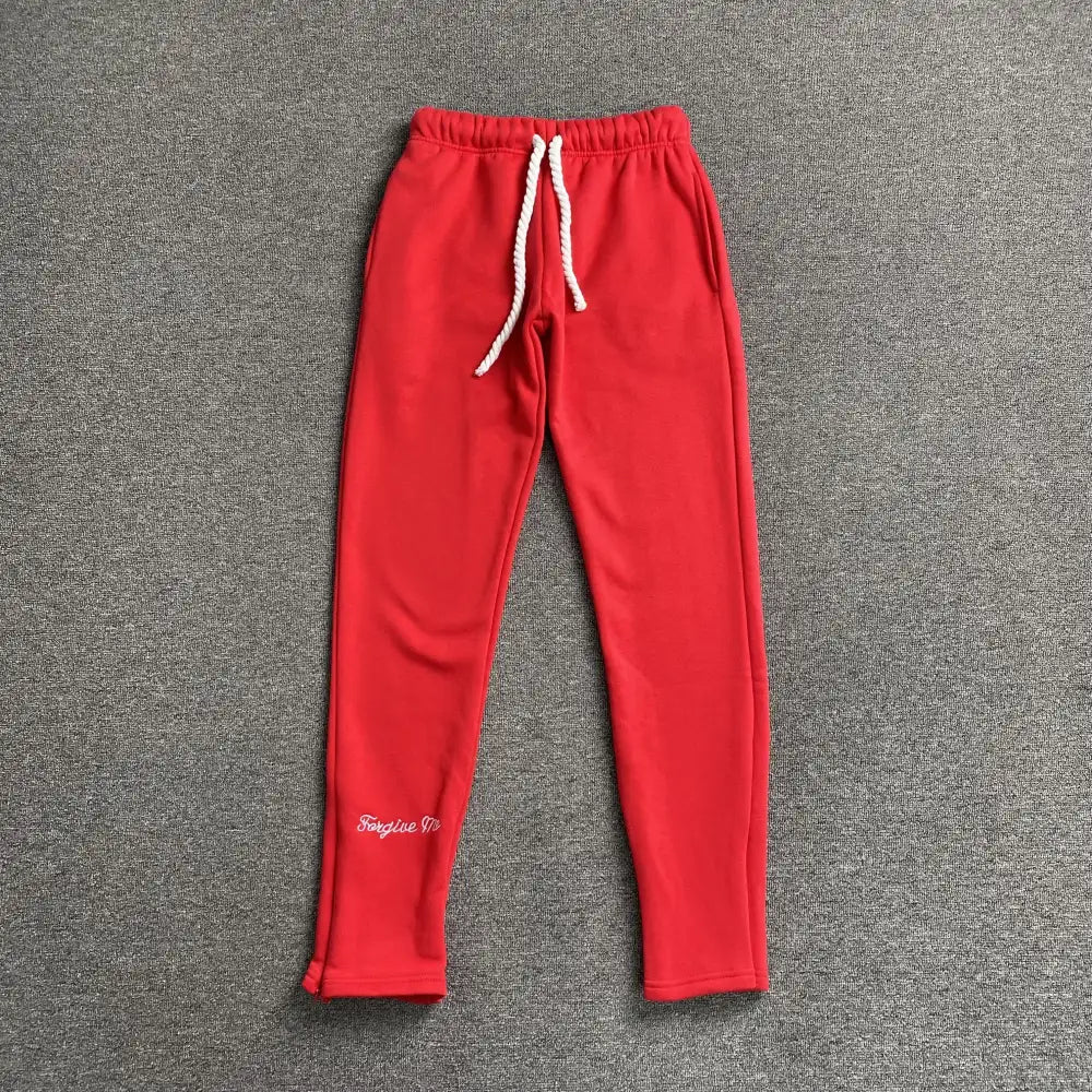 Red Syna World jogger pants laid flat, showing white rope drawstring and script embroidery on lower left leg