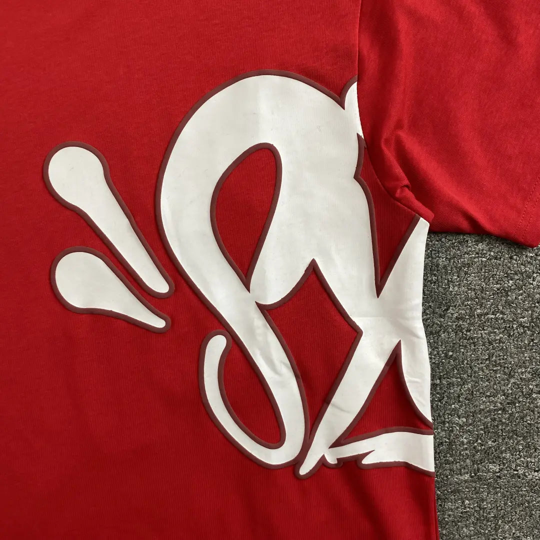The Syna World Red Letter Print Crew Neck T-Shirt features bold white graphics with curved lines extending from front to side, giving this streetwear cotton tee a unique look. Shown laid flat on a gray textured surface.